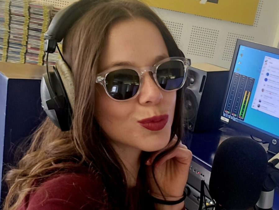 Lisa Laner mit Kopfhörern und Sonnenbrille im Studio von Radio Holiday, vor ihr Mikrofon und Mischpult.