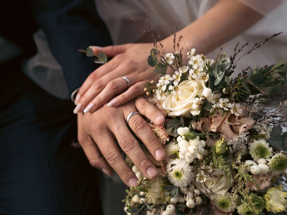 Zwei Hände liegen auf einem Brautstrauß aus hellen Blumen, Beispielbild von Südtirol Wedding.